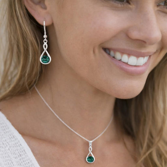 Woman wearing a silver necklace and earrings with green gemstones.